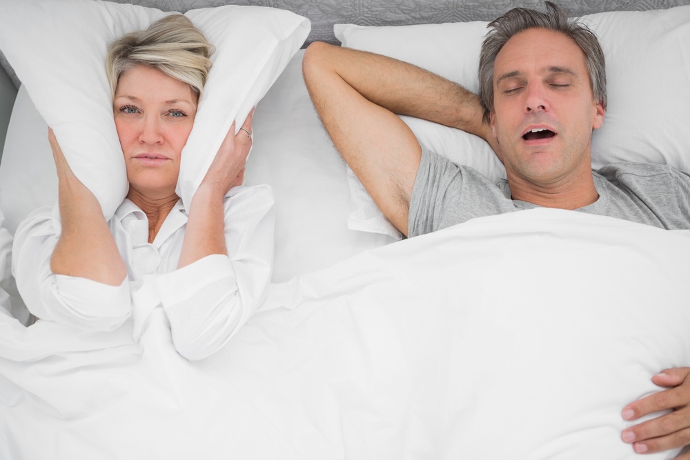Man snoring loudly as partner blocks her ears at home in bedroom